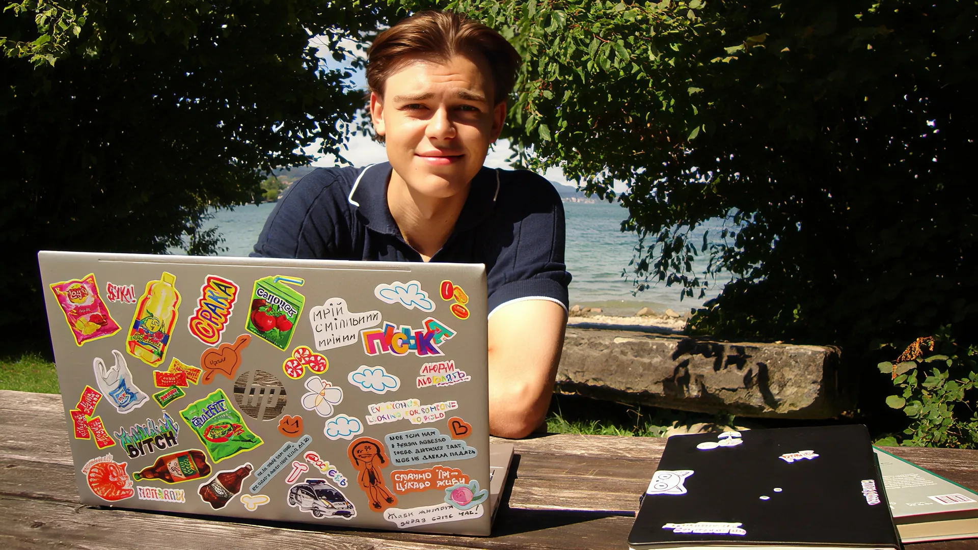 Luka Ivanyshyn at a lakeside table with a laptop covered in stickers